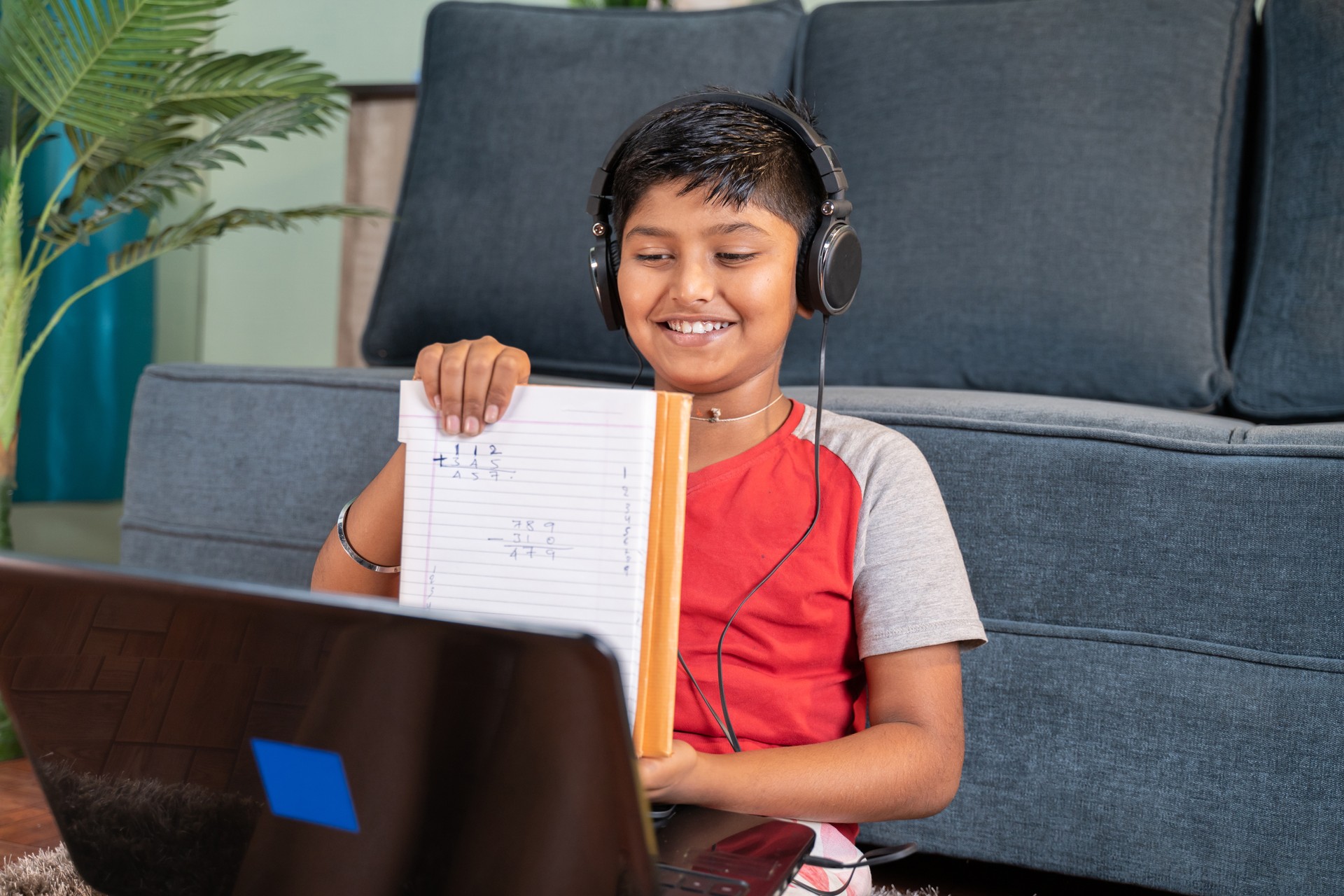 Kid interacting during online class by showing solved problems to tutor on laptop - concept of new normal virtual education and e-learning due to covid-19 pandemic.